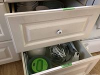 Open drawer showing vintage Sunbeam Mixmaster mixer with beaters and accessories along with plastic bowls and other kitchen items