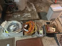 Electrical cords, extension cords, wire baskets, and mouse traps displayed on basement floor next to water heater.