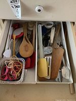 Top-down view of kitchen drawer with various utensils including whisks, wooden spoons, silicone spatulas, and metal spoons