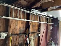 Full view of the 24-foot aluminum ladder mounted horizontally on a wooden garage wall with other tools hanging below.