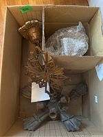 Top-down view of the light fixture inside a cardboard box, showing the metal body with multiple bulb sockets and part of the glass shades wrapped in bubble wrap.