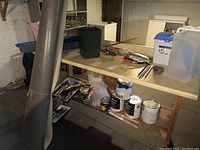 Workbench area with paint cans, tools, storage boxes, and large roll of vinyl in basement