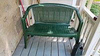 Plastic green patio bench placed on a painted wood porch floor, showing right side and front view.