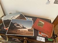 Two large landscape photo prints and a red album labeled 'POST CARDS' on a black trunk