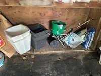Wide view of four plastic planters, Scotts spreader, and multiple garden supply bags on wooden floor in garage.