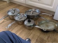 Full view of the set on the floor including pots, pans, lids and cast iron fry pan