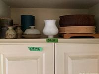 Wide shot of shelf showing all ceramic pottery, white milk glass lamp shade, and wooden bowls arranged in a row.