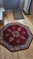 Two rugs placed on hardwood floor: one octagonal red floral rug and one smaller rectangular beige floral rug near entrance door.