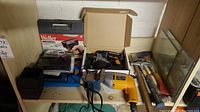 Photo showing bench vice, Weller soldering kit, staple gun, hammers and yellow power drill on a wooden shelf.