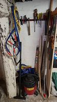 Photo showing jumper cables, vintage hand tools like screwdrivers and hammer hung on a wall, shop vacuum cleaner at floor level near wall