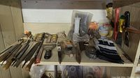 Wide view of the shelf showing metal files, paint scrapers, gloves, measuring tape, and putty knives.