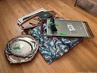 Wood trays, silver plated trays and coasters, dragonfly printed fabric placemats all stacked on a wooden floor.