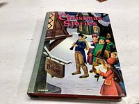 Front cover of 1940 hardcover book titled 'Christmas Stories' showing festive illustration of carolers by 'Ye Olde Bakery' sign.