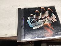 Front of CD case with album artwork showing hand holding a razor blade with Judas Priest logo and British Steel text.
