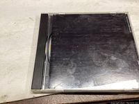 Closed view of the CD jewel case showing black album cover insert with scratches on case but no scratches on CD confirmed later.