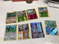 Eight holographic Pokémon cards arranged on a white surface, showing various characters and foil designs.
