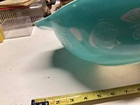 Close-up of the spoon-like pouring spout end of the teal Pyrex bowl with portion of the hot air balloon design visible and measuring tape for scale.