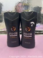 Two new bottles of AXE Dark Temptation Body Wash placed side by side on a pink surface with a reflective background. One bottle has minor label wear.