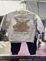 Photo of new baby outfit size 0-3 months featuring Star Wars Grogu (Baby Yoda) graphic sweatshirt with text 'Cutest in the Galaxy' and black pants, with tags attached.