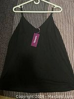 Front view of black Hello Baby tank top on white plastic hanger against striped fabric background.