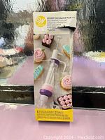 Front of box showing Wilton Dessert Decorator Plus with decorative cupcakes and count of accessories included.