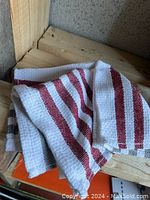 Three dish cloths, two with red stripes and one with black stripes, folded and placed on a wooden surface.