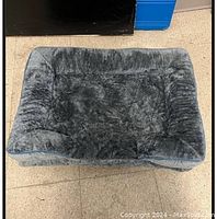 Gray plush dog bed captured on tiled floor, showing cushioned sides and soft furry surface.