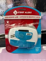 Front view of First Alert carbon monoxide alarm in red and blue damaged packaging showing the product and branding.