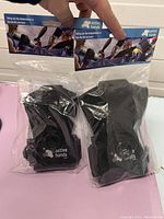 Photo showing two black Active Hands hand grips in sealed clear plastic packaging with branded header cards, held by hand.