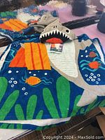 Full view of hooded towel laid flat showing colorful oceanic prints, shark hood, and attached tags.