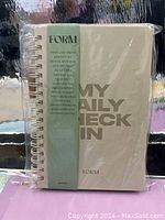 Front view of new spiral-bound fitness and wellness daily check-in book titled 'MY DAILY CHECK IN' with a green wrap band