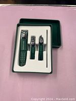 Photo of a new manicure set containing three nail clippers of different sizes and one metal file in a green plastic box with white foam insert.