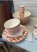 Photo showing stacked large and small bowls, plates, and cups with orange and white plaid pattern