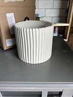 Front and side view of the off-white ceramic planter showing vertical ribbed design and scalloped edge