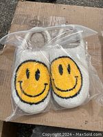 Photo of the slippers in clear plastic packaging showing the smiley face designs.