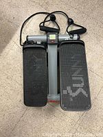 Top view of the Sunny Step Machine showing textured foot pedals, central digital display, and attached resistance bands with handles.