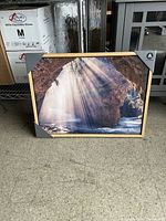 Canvas print with photo of sun rays through rock formation, light wooden frame, protective corner guards on canvas.