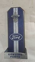 Full view of blue metal wall-mounted bottle opener with Ford logo and Genuine Parts text on bottom cap catcher.