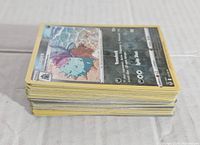 Stack of approximately 50 random Pokémon cards laid flat, showing card edges and yellow borders