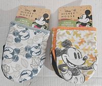 Photo of two new Disney Mickey Mouse oven mitts with tags, one with a repeating Mickey Mouse pattern and the other with a large Mickey Mouse image and leaf designs.