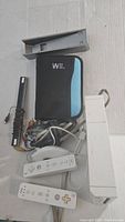 Full lot display showing Nintendo Wii console, two Wii Remotes, sensor bar, AV cables, console stand, game case, and Nunchuk attachment