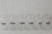 Photo showing all six identical Heineken glasses in a row, clear glass with gold rims and colored logos.