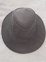 Top view of brown oilskin leather Australian style hat with rounded crown and wide brim, showing leather texture and braided band detail.