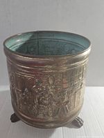 Side view showcasing the embossed brass surface with detailed scenes and small feet at base.