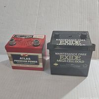 Two vintage car battery shaped radios: red and white Atlas Premium Power and black Exide Mega Cell Gold.