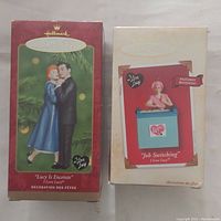 Two I Love Lucy Hallmark ornament boxes side by side, one labeled 'Lucy Is Enceinte,' the other 'Job Switching' with movement feature.