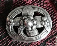 Front view of oval sterling silver brooch featuring central floral medallion with leaf motifs and open oval frame
