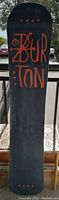 Base side of the snowboard showing black surface with orange Burton logo