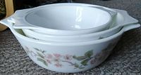 Photo showing stack of three white ceramic casserole dishes with Cherry Blossom pattern from side view revealing floral design and handles.