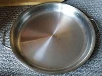 Large round stainless steel pan with handles, used for roasting or cooking, showing some wear.